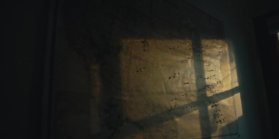 Light from window casts shadows on map stuck with pins that hangs on wall
