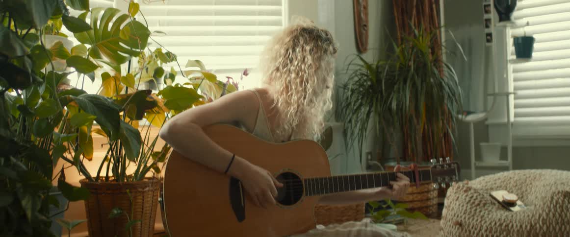 A teenage girl sits at home and plays the guitar