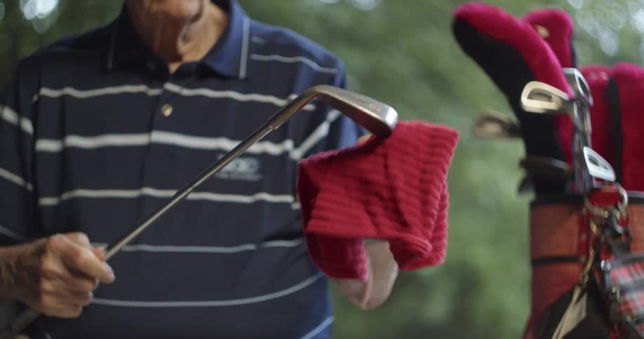 Elderly man with blue polo shirt cleans golf club