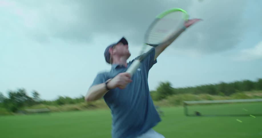 Man energically practicing tennis swings on a field outdoors