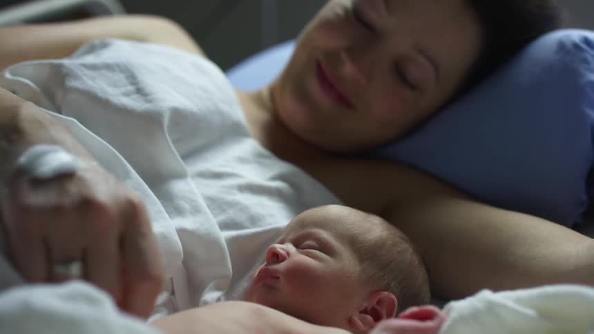 A woman and a baby in a room laying in a bed with a wall in the background