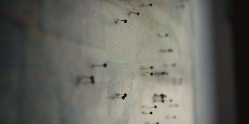 Pins over a map hanging from a wall inside a dimly lit room
