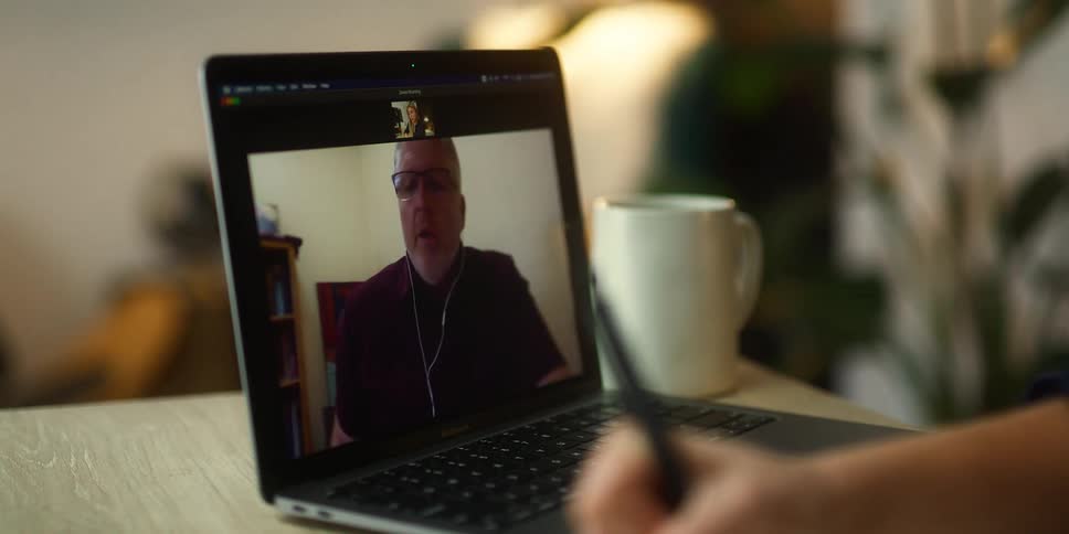 Person takes notes while watching a man talking on a video on a laptop