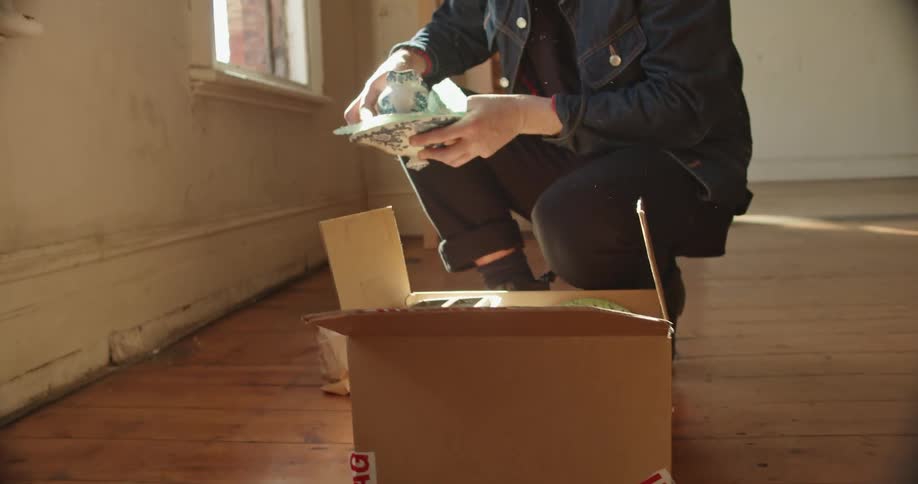 A man unpacks a single box removing a china gravy boat in a bright sunny apartment