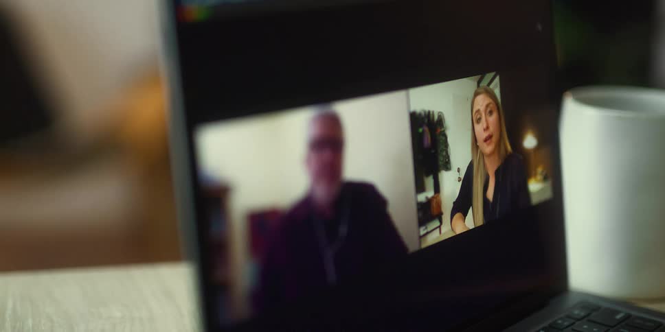 Two people talking on a video call on a laptop screen over a desk
