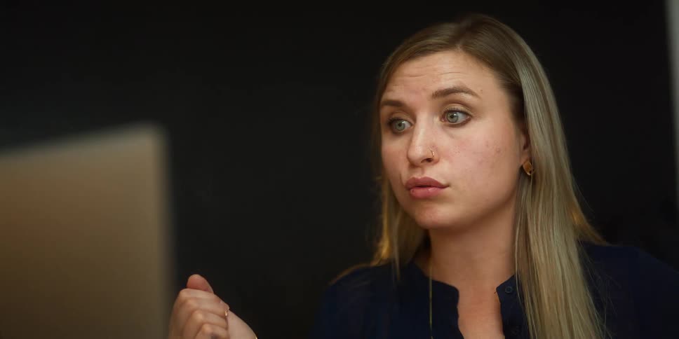 Woman with long hair motions with her hand while talking and looking at a laptop