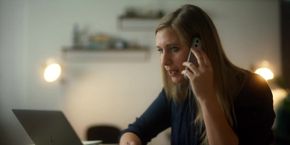 A woman scrolling on a laptop while talking on a phone in an office setting