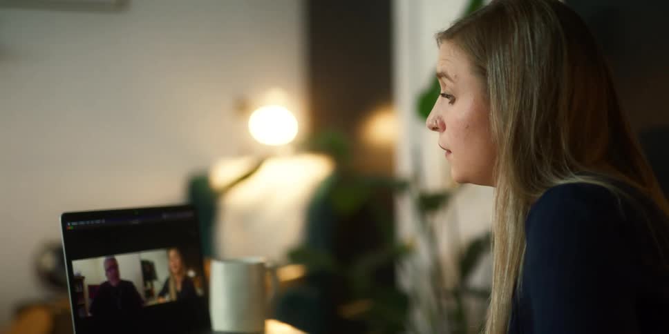 A young woman uses a laptop to participate in a video chat with an older man while sitting at a table at home