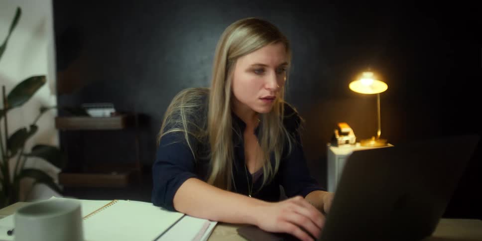 A young woman sits at a desk in an office and works on her laptop