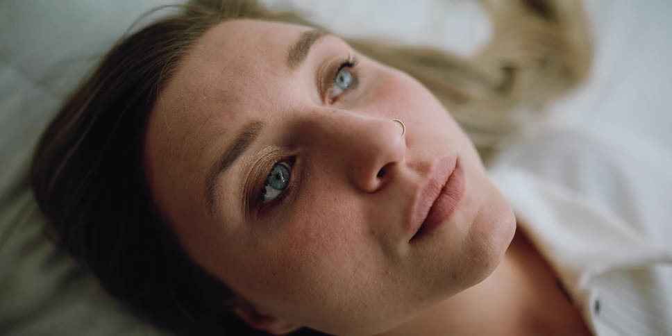 A woman is blinking and staring upwards while laying down