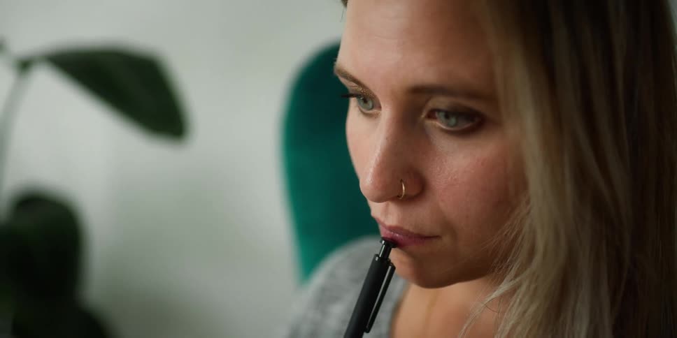 A woman in an office taps a pen on her lip as she thinks
