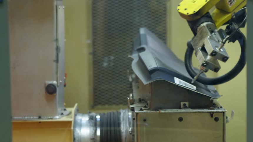 A robotic machine cuts or assembles an item on a stand