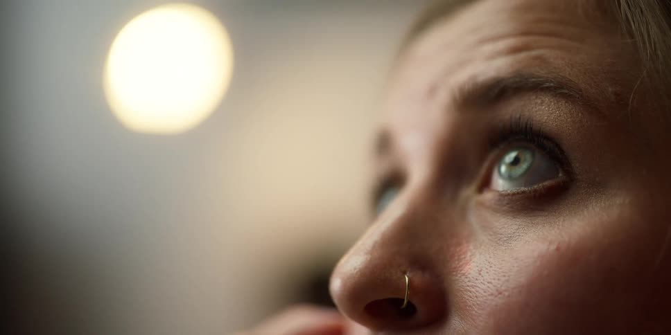 Woman wearing a nose ring blinks her eyes as she looks up towards the ceiling