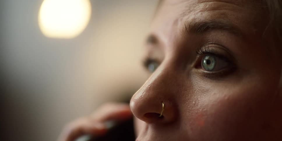 Blonde woman with blue eyes and nose ring talks on smartphone