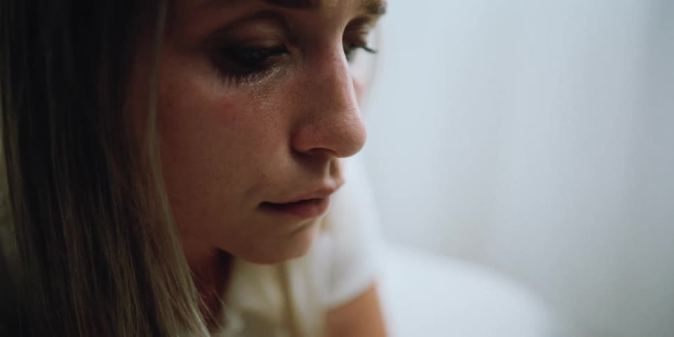 Close up of a sad woman sitting on a bed crying inside a white room