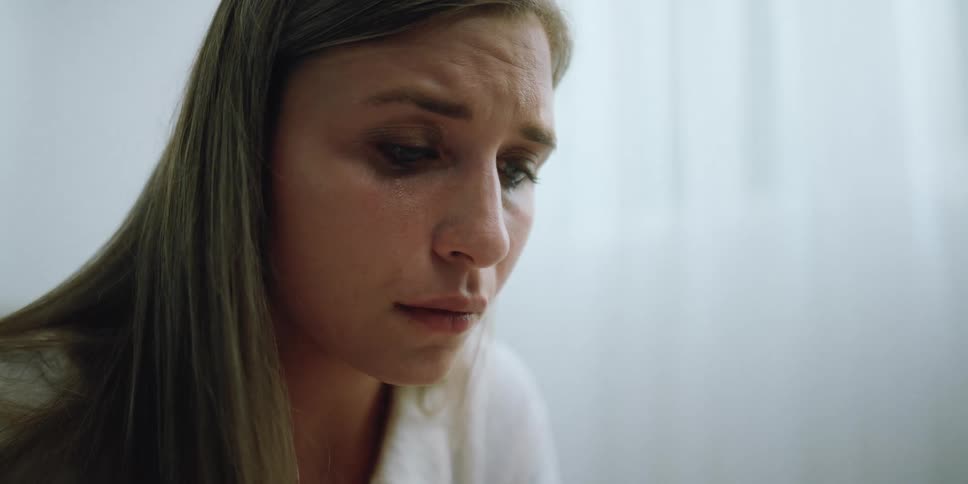 A woman in a room crying with tears falling from her eyes with a wall in the background