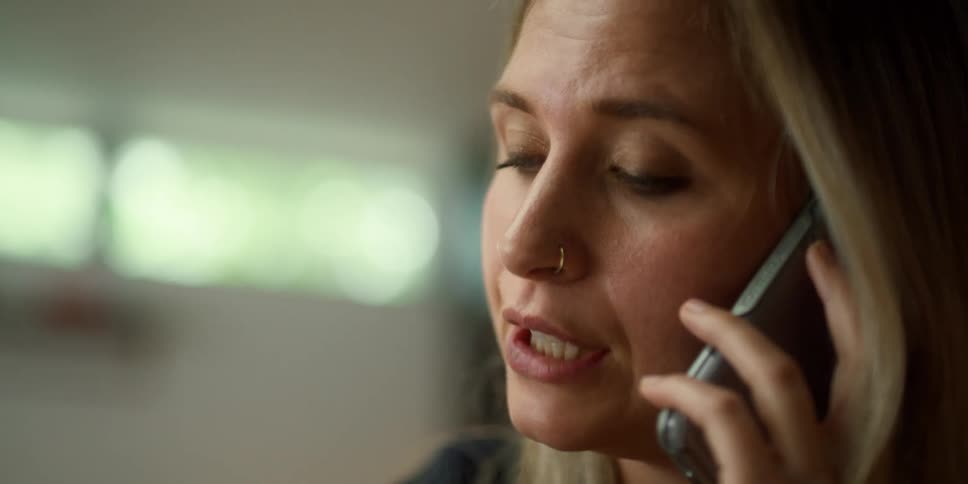 Blonde woman with blue eyes and nose ring talks on smartphone