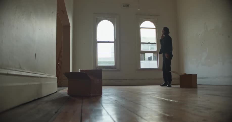 Man with denim jacket and black pants talks on smartphone in empty room