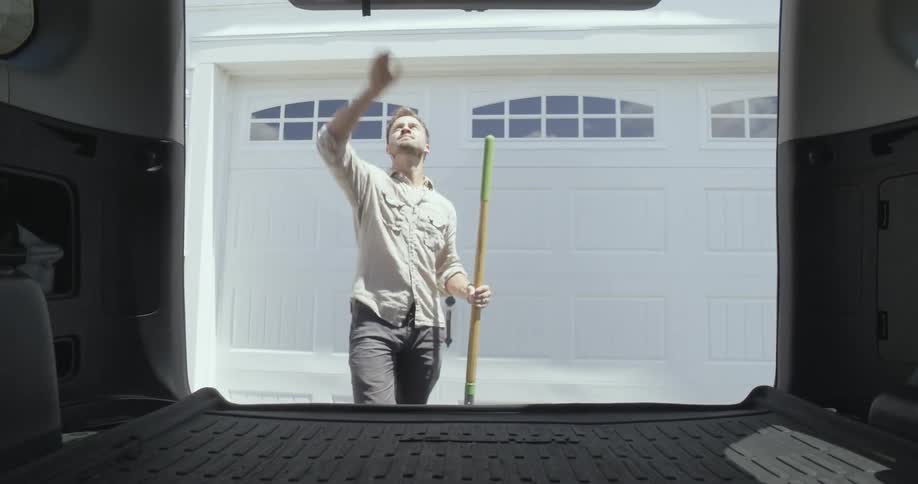 A man receives a shovel from the back of a van parked in a driveway before closing the backdoor of the vehicle