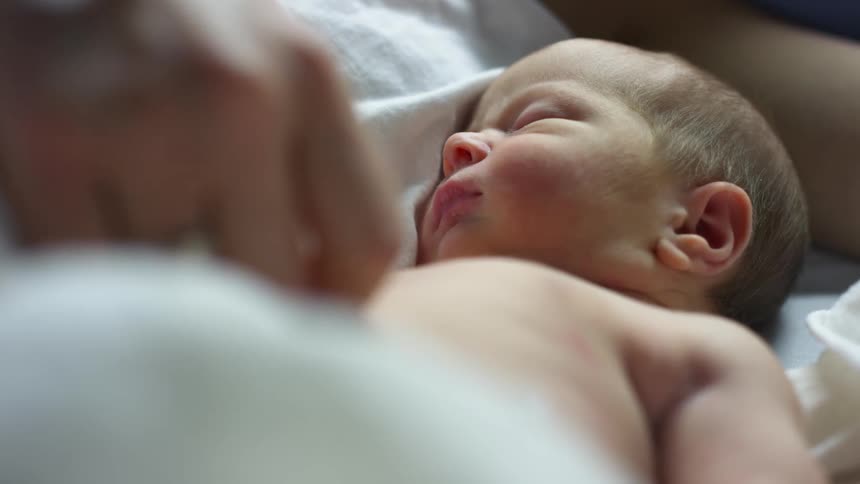 A person in a room caressing a baby stomach as he sleeps