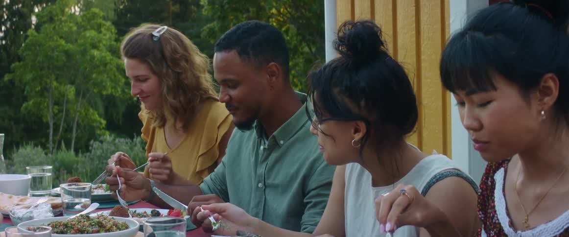 Friends sit outdoors at picnic table talking and eating