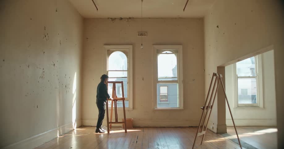 Man places an easel next to a window inside an empty apartment and takes a picture of it with a smartphone