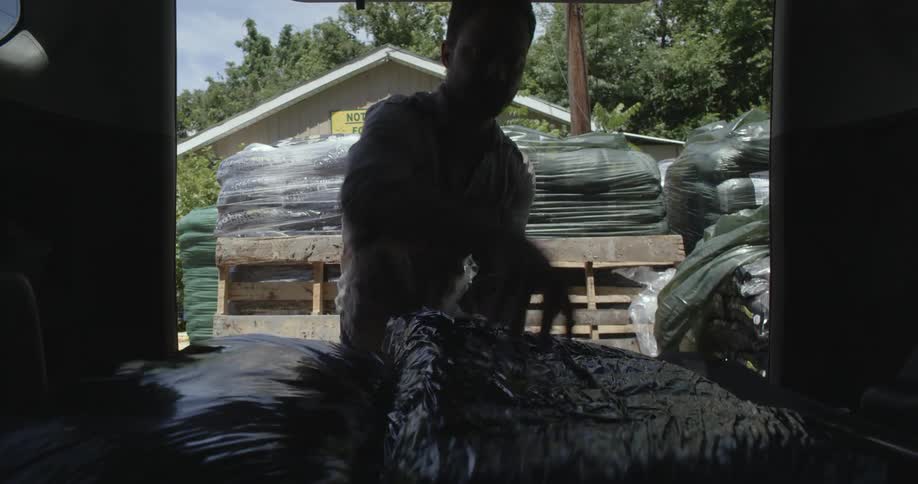 Man loads bags of soil and mulch onto back of vehicle at garden store