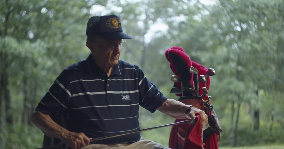 A man sits outside and wipes down his golf clubs