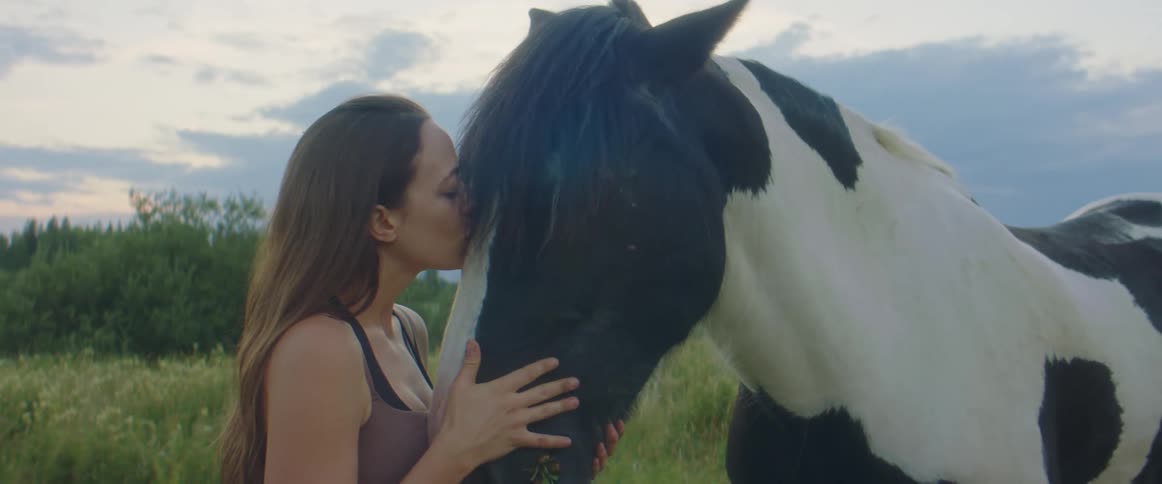 A young woman caresses the nose of her horse as she kisses it and talks to it
