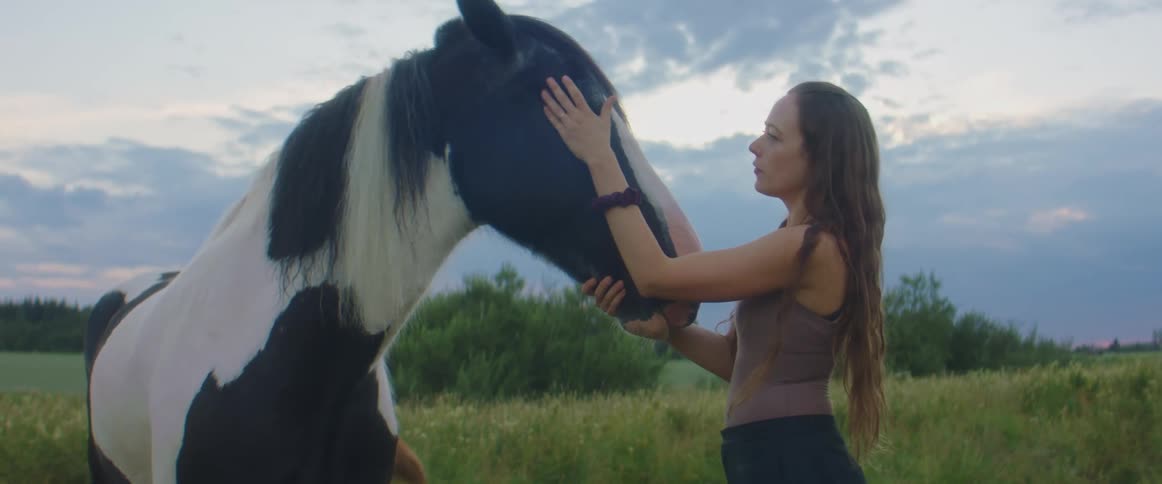 Woman stands next to horse in pasture petting it