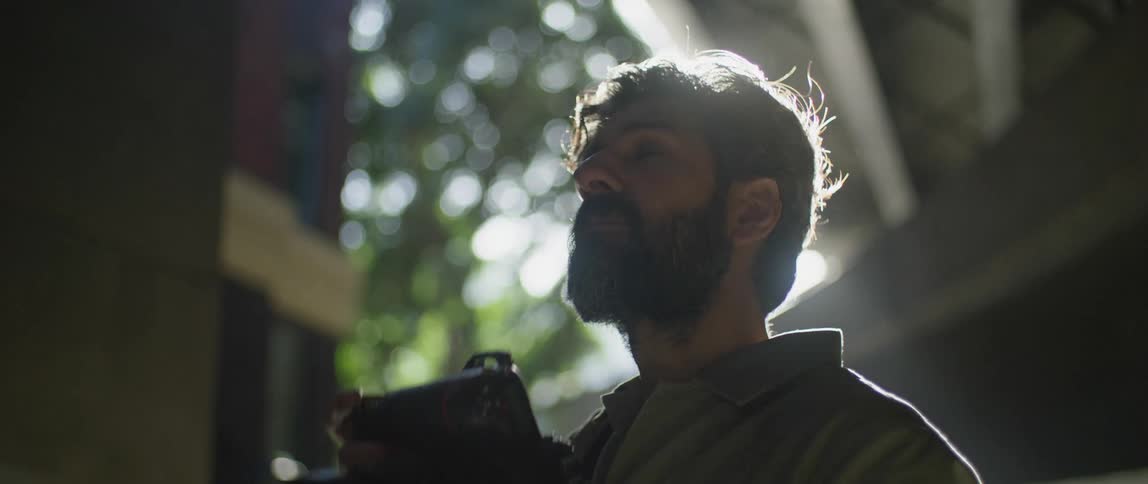 A man with a camera underneath an overpass with the sky and clouds in the background