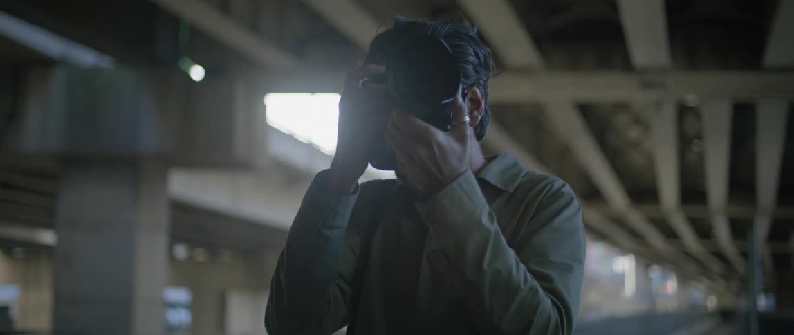 A photographer adjusts his camera and takes a photograph while standing under a bridge