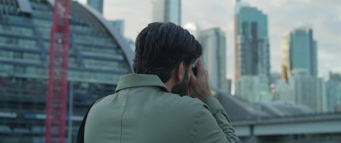 A man raises a camera to take a photograph of the skyscrapers of a metropolis in the evening