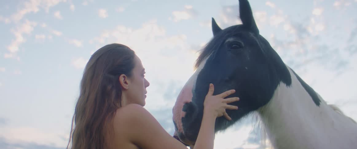 Woman stands outdoors petting horses face under cloudy blue sky