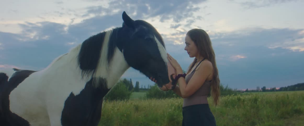A woman stands outside beside a horse and kisses it on the head