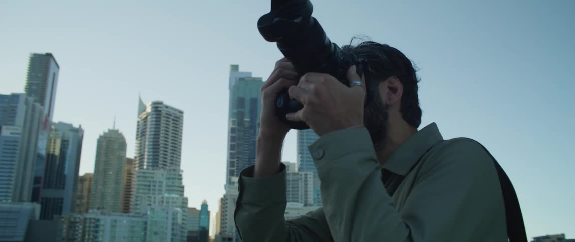 Male photographer with shirt and beard takes photographs of high rise buildings in the city
