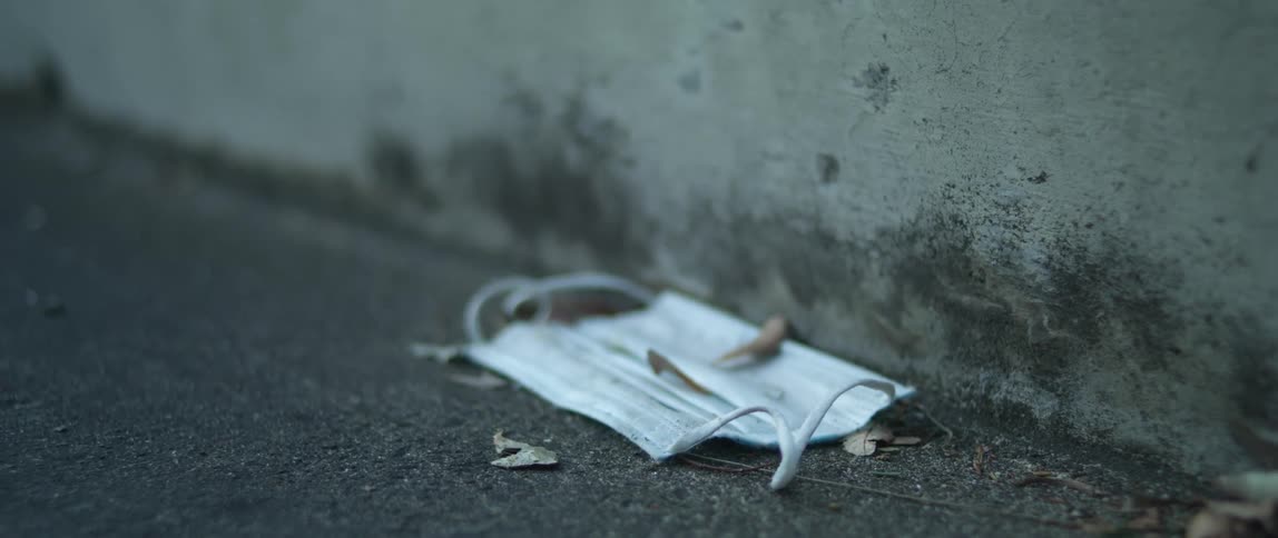 A used medical mask lying in the road next to the curb