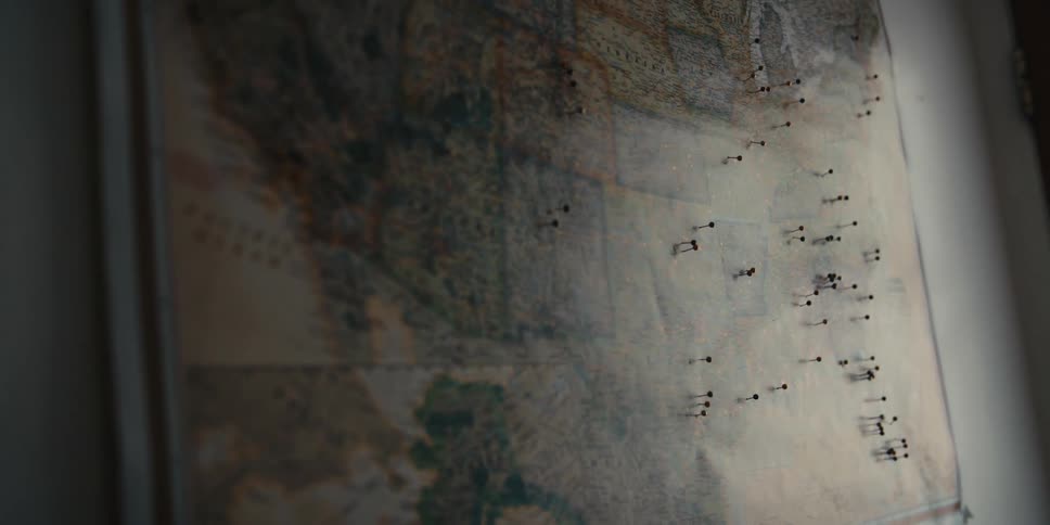 Map with several pins hanging on a wall inside a dimly lit room
