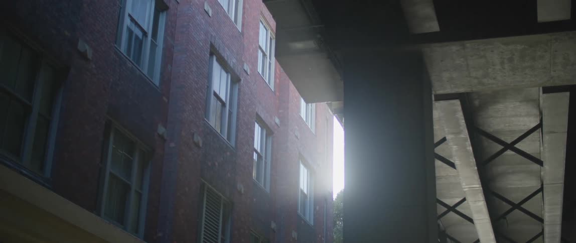 Sunlight filtering between a building and a bridge in the city at morning