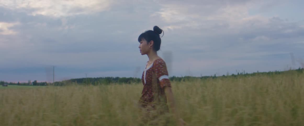 An asian woman walking through a field of tall grass