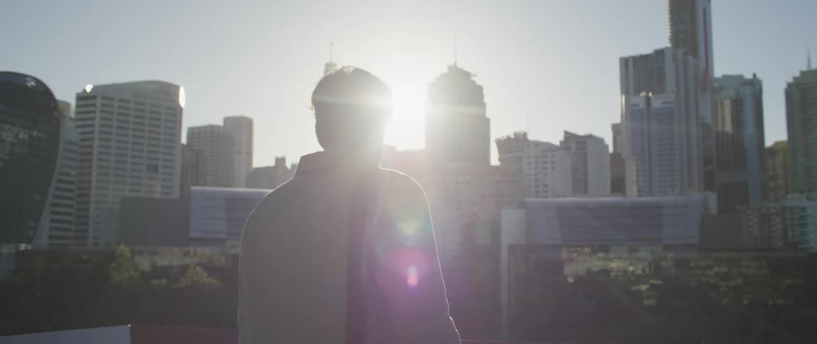 A man walking in a city with the city skyline buildings skyscrapers the sky and clouds in the background