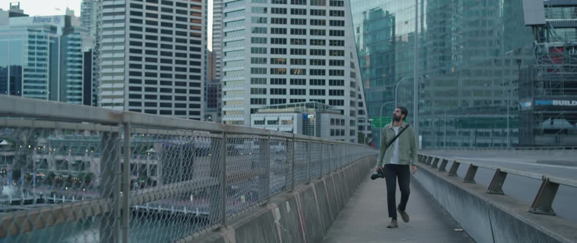 Man carrying a camera walks on a bridge over a river in the city