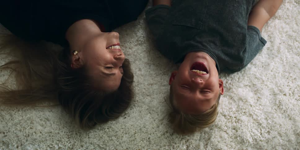 A mother and young son smiling and laughing while lying on carpet