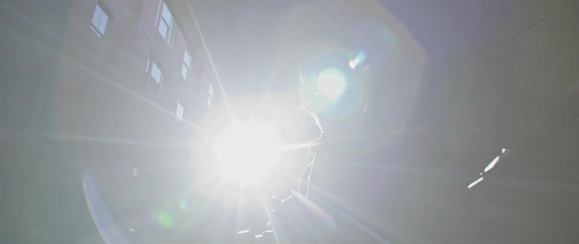 A man standing beneath a city bridge with bright sunlight behind him