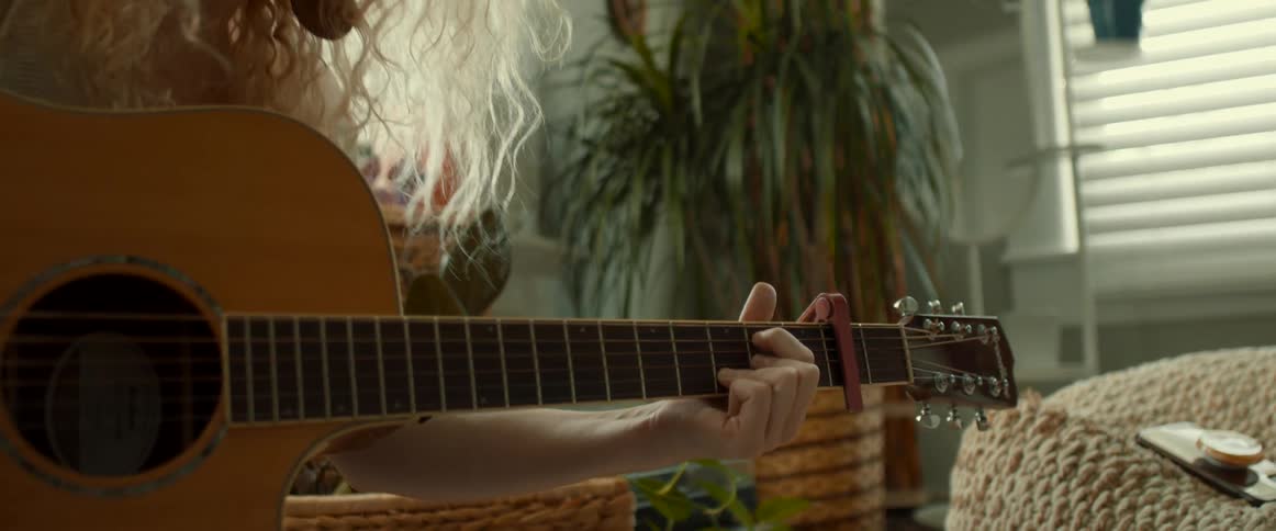 Blonde woman with wavy hair and earrings plays guitar while singing a song