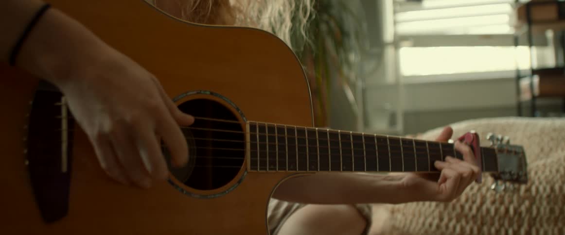 Blonde woman with wavy hair plays guitar in the living room at home