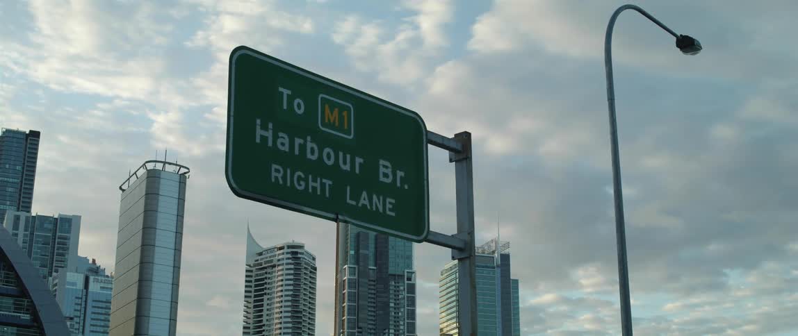 A street sign with tall skyscrapers in the distance on a cloudy day