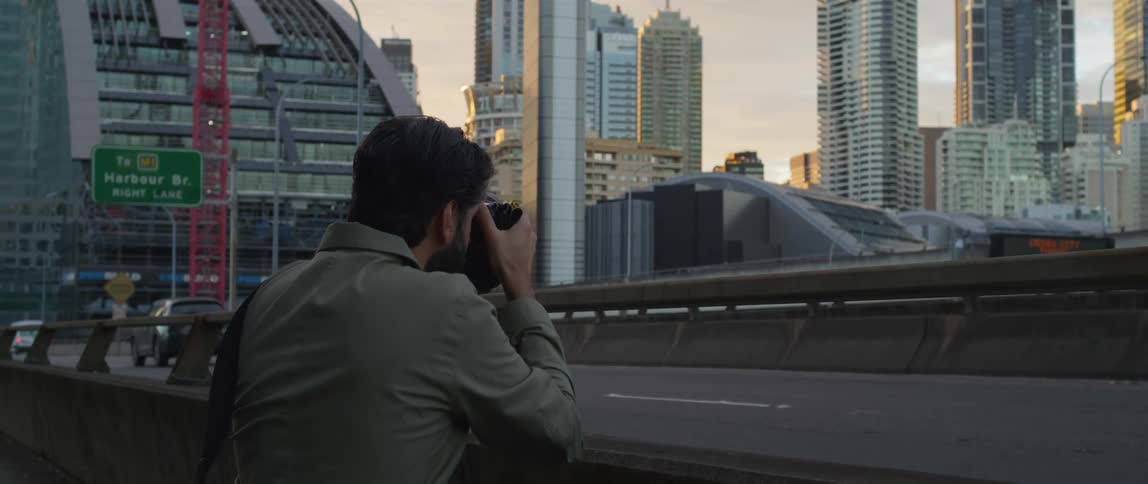 A man with a camera taking a picture of the city skyline with buildings skyscrapers the sky and clouds in the background