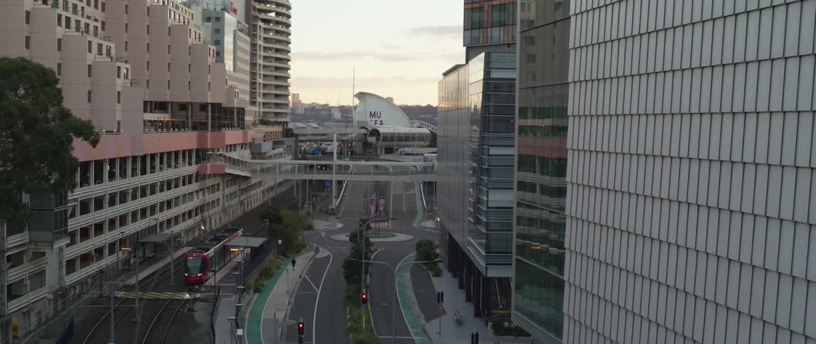 Train travels on the tracks in the city as a pedestrian walks on a sidewalk