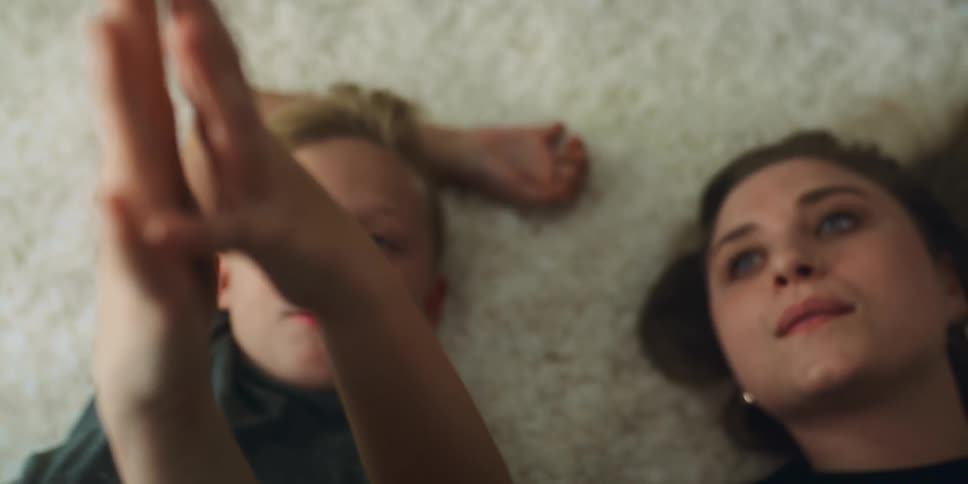 A mother and son touching hands while lying on a carpeted floor at home